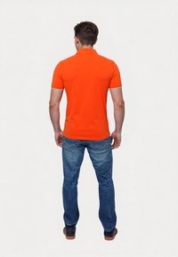 Orange pikétröja med korta ärmar, med en kontrasterande turkos kant på kragen och ärmarna. Bärs med blå denimjeans.
