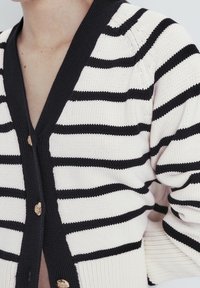 Sweter w paski w kolorze kremowym i czarnym, z głębokim dekoltem w kształcie V, ściągaczami przy mankietach oraz złotymi detalami w postaci guzików. Gładka tekstura i luźny krój.