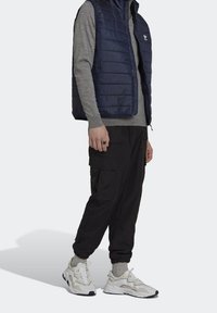 Navy padded vest, gray long-sleeve shirt, black cargo pants, and white sneakers with gray accents. Textured materials, layered design.