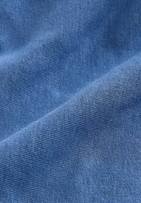 Gros plan sur un tissu bleu doux et texturé avec un motif de tricot visible et des plis délicats créant des ombres et des lumières.