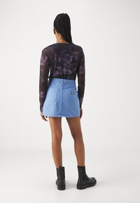 Jupe en denim bleu clair avec une taille haute et deux poches arrière, associée à un haut noir en tie-dye à manches longues et des bottines noires.