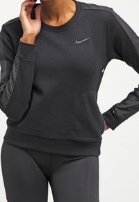 Sudadera negra con mangas largas, hecha de material suave. Presenta un cuello redondo, el logo de Nike y sutiles acentos de malla en las mangas.