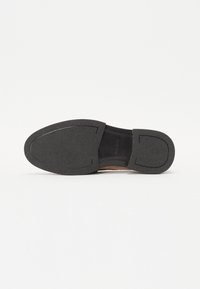 Semelle de chaussure en caoutchouc noir avec surface texturée, présentant un profil bas et une forme arrondie. Comprend des lignes de design subtiles et un marquage de la marque.