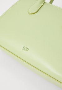 Sac à main vert menthe en matériau brillant, avec un logo en relief, des coutures décoratives et une forme épurée avec une fermeture à rabat.