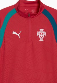 Maillot de sport rouge avec des bandes latérales bleu sarcelle, logo Puma sur la poitrine gauche, blason de la fédération de football du Portugal sur la droite, et un col avec fermeture éclair au quart.