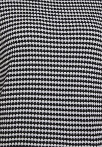 Tessuto lavorato a maglia in bianco e nero con un motivo testurizzato di piccoli triangoli alternati che creano un design a griglia.