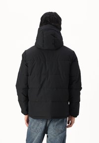 Chaqueta de plumas negra con capucha desmontable, diseño acolchado, textura suave y puños elásticos, combinada con jeans de mezclilla azul claro.