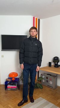 Μαύρο φουσκωτό μπουφάν με ψηλό γιακά, που διαθέτει οριζόντια ραφή. Συνδυασμένο με σκούρες μπλε παντελόνες και γυαλιστερά παπούτσια. Εσωτερικός χώρος.