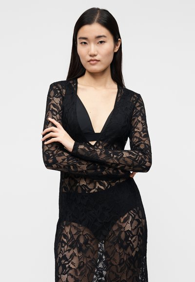 Juodas nėriniuotas viršus su ilgomis rankovėmis ir giliu V formos iškirpte. Turi gėlių raštą ir permatomą tekstūrą, atskleidžiančią juodą vidinį drabužį.