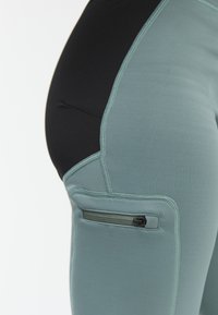 Sport leggings met een slanke pasvorm, met een mintgroene voorkant en een zwarte achterkant, zijzak met rits en contrasterende stiksels.