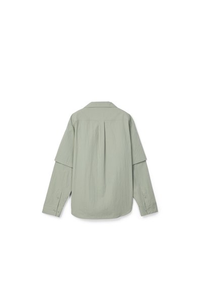 Camisa de manga larga gris claro con pliegue en la parte trasera y puños abotonados, vista desde atrás sobre un fondo blanco.