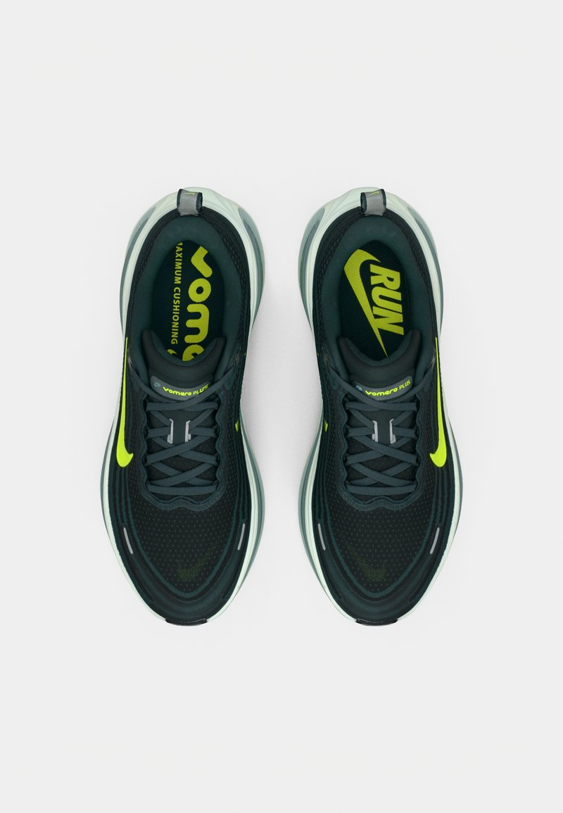 Un par de zapatillas de running negras y verde neón con suelas blancas gruesas, cordones visibles y plantillas de marca en negrita que dicen "Vomero Plus" y "RUN".