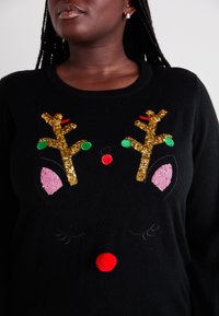Schwarzer Pullover mit einem Rentierdesign, das goldene Geweihe, pinke Ohren, grüne und rote Verzierungen sowie eine rote Pompon-Nase aufweist.