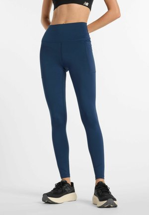 Navy blue high-waisted leggings with smooth, stretchy fabric; features a side pocket and contrasting black sneakers with a textured sole.