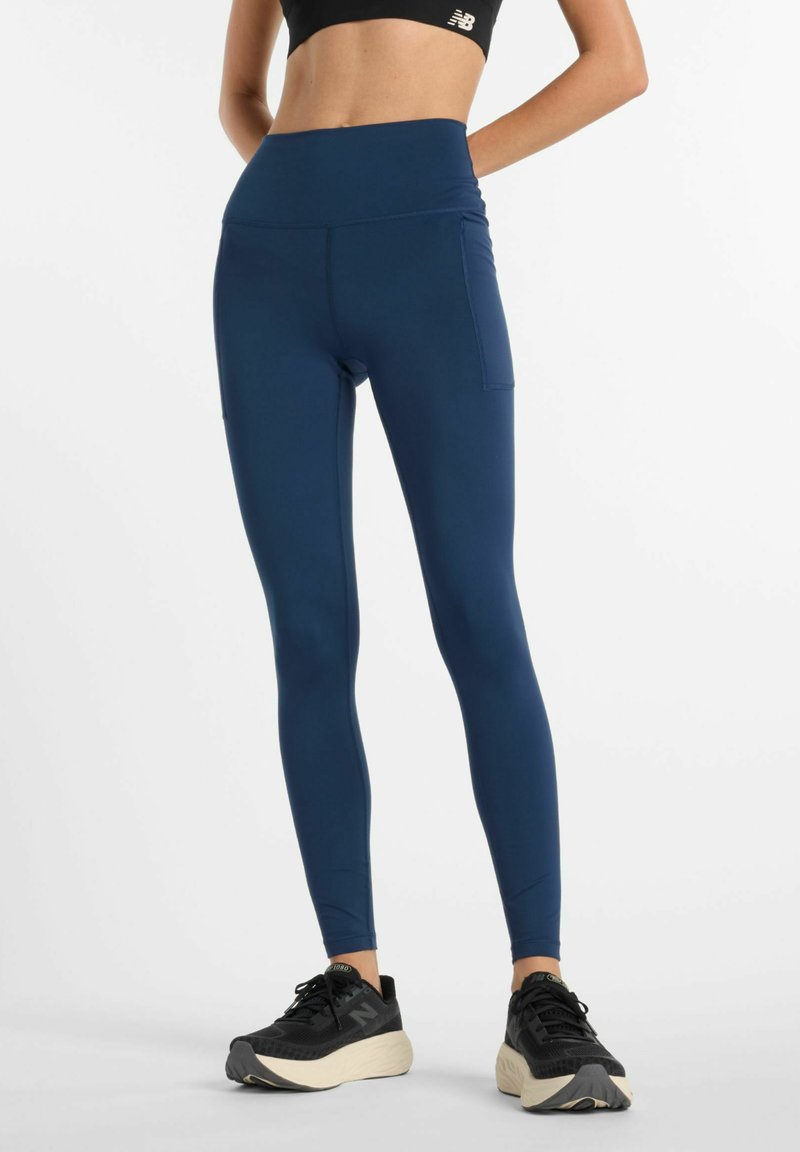 Leggings a vita alta di colore blu navy realizzati in tessuto liscio ed elasticizzato; presentano una tasca laterale e sneakers nere a contrasto con suola testurizzata.