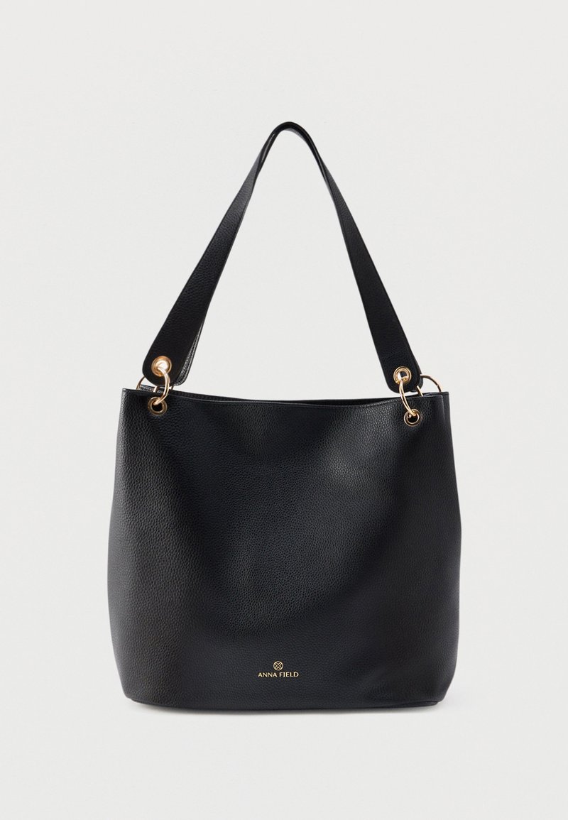 Sac cabas en cuir noir avec une finition texturée, des accents de ferrures dorées et deux bretelles d'épaule. Logo visible en bas à l'avant.