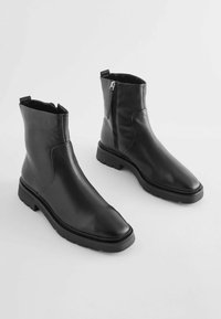 Bottines noires en cuir avec un bout carré, finition texturée, fermeture éclair sur le côté et semelle en caoutchouc épaisse. Extérieur lisse avec un minimum de détails.