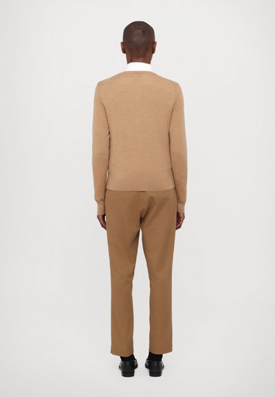 Tan sweater made of soft fabric, round neck, and ribbed hem paired with matching tan trousers. Black shoes and white collar detail visible.