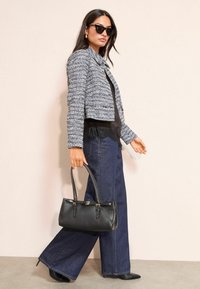 Szary żakiet w kratę o skróconym kroju, czarna bluzka z koronkowymi wykończeniami, szerokie dżinsy oraz czarna torebka z złotymi akcentami.