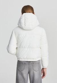 Biała kurtka puchowa z odpinanym kapturem, pikowany design, elastyczny pas i mankiety. W połączeniu z szarymi dżinsami.