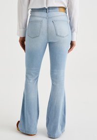 Light blue flared jeans featuring back pockets and a waistband with a logo patch. The fabric shows a slight fade and smooth texture.