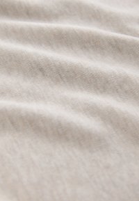 Tissu doux beige clair avec une texture tissée subtile et des plis doux créant une surface lisse légèrement ondulée.