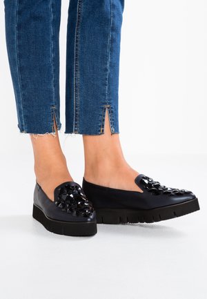 Bottines noires à enfiler avec une semelle épaisse, présentant un accent clouté sur le bout et une texture en cuir lisse. Associées à un denim raccourci.