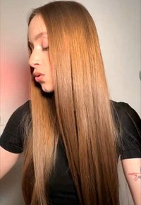 Jeune femme aux longs cheveux roux lisses portant un haut noir, regardant vers le bas et sur le côté sur un fond clair uni.