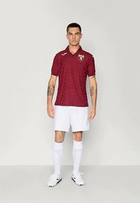 Μαρέν κοντομάνικο φανελάκι ποδοσφαίρου με υφασμάτινη υφή και σήμα ομάδας; συνδυασμένο με λευκή βερμούδα και λευκές κάλτσες μέχρι το γόνατο.