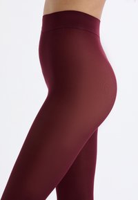 Leggings bordeaux con una texture liscia e elasticizzata, vita alta e design aderente, che mette in risalto una silhouette snella.