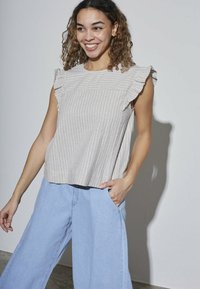 Lys grå stribet bluse med flæser på ærmerne, parret med vide lyseblå denimbukser, der fremhæver et afslappet design og løs pasform.