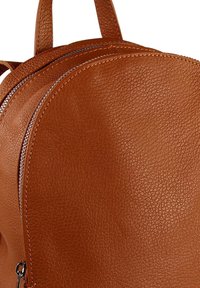 Bruine leren rugzak met een gestructureerd oppervlak, een ronde bovenkant en een dubbele ritssluiting, waarbij een deel van de handgrepen zichtbaar is.