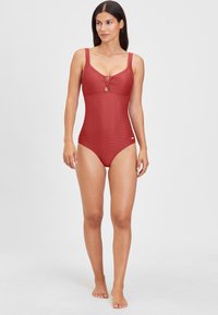 Maillot de bain une pièce rouge avec texture côtelée, larges bretelles, un détail en trou de serrure au niveau de la poitrine et un petit logo près de la hanche.