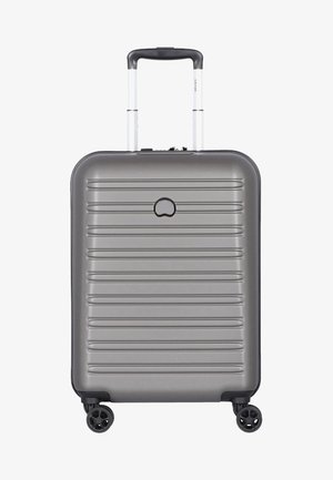 Hard-shell, gray suitcase with a ribbed design, telescopic handle, and four black wheels. Features a minimalist logo on the front.