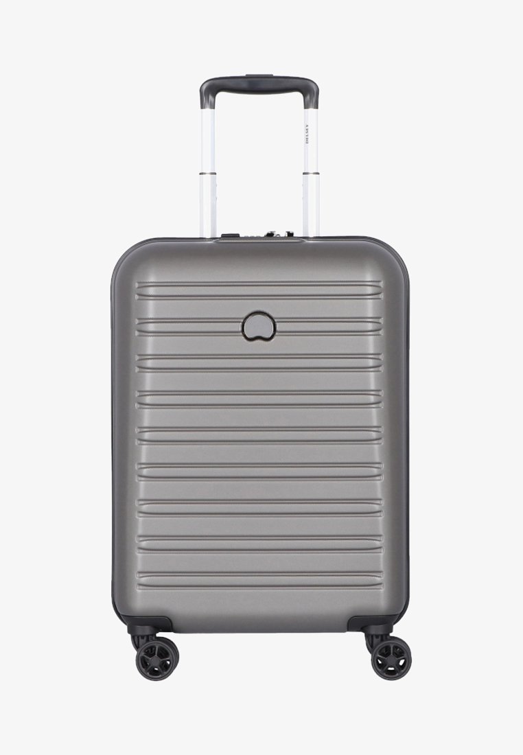 Hard-shell, gray suitcase with a ribbed design, telescopic handle, and four black wheels. Features a minimalist logo on the front.