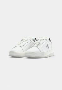 Sneakers bianche in pelle con punta tondeggiante, branding discreto, dettagli neri sul tallone e suola in gomma testurizzata. Lacci passati attraverso occhielli.