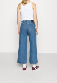 Ljusblå vida jeans med hög midja, med en klassisk femfickedesign. Bakfickorna är broderade med detaljer. Kombinerade med vita strumpor och vinröda sneakers.