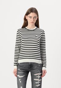 Svart og hvitstripet genser med rund hals og ribbede mansjetter, sammen med slitte grå denimbukser.