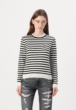 Un pull à rayures noires et blanches avec un col rond et des poignets côtelés, accompagné d'un jean en denim gris déchiré.