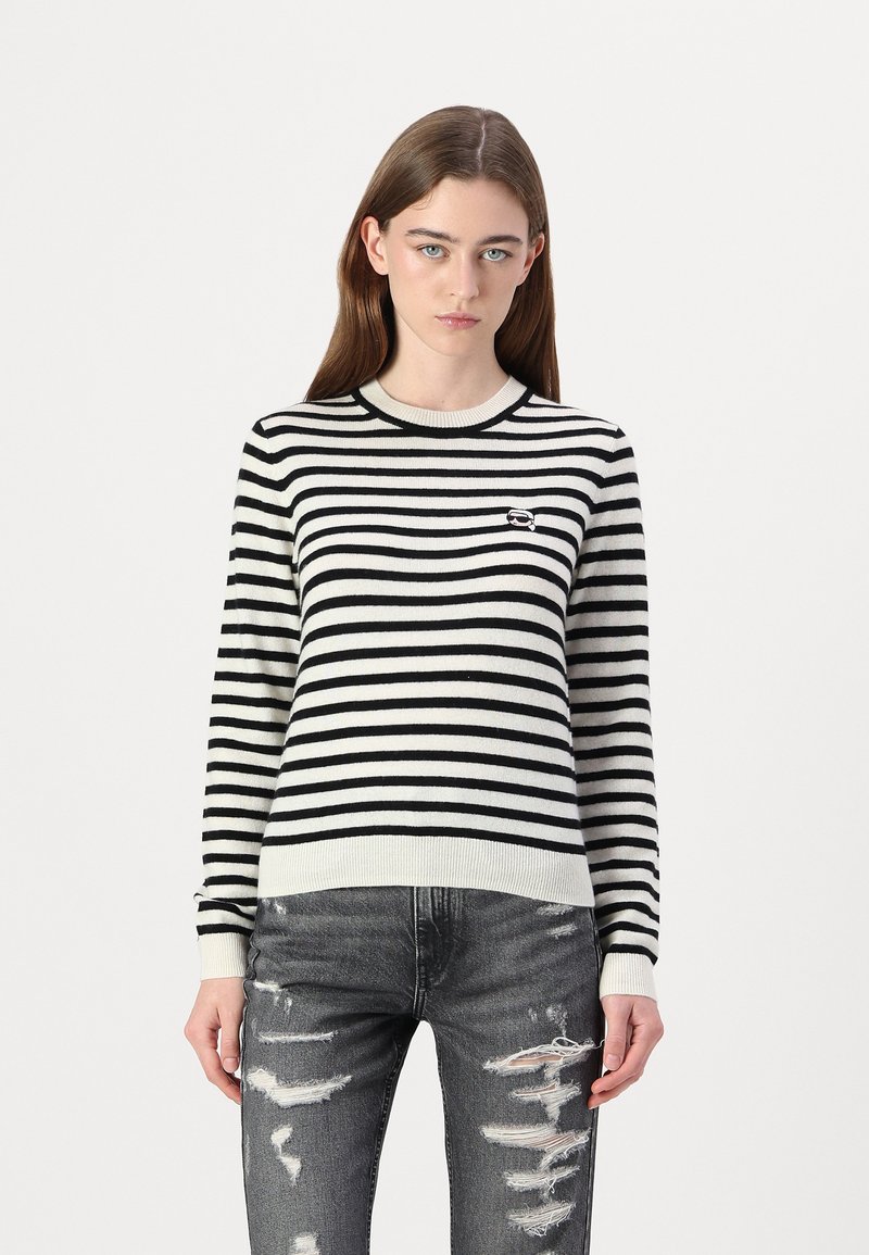 Svart og hvitstripet genser med rund hals og ribbede mansjetter, sammen med slitte grå denimbukser.