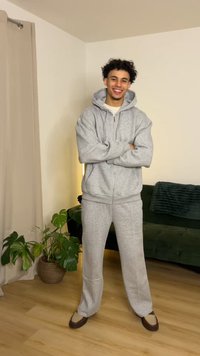 Gray hoodie and sweatpants set in soft fabric, featuring a zip closure, relaxed fit, and ribbed cuffs. Worn with brown slip-on shoes.