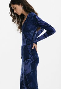 Pikk tumesinine kleit ribakujulise tekstuuriga, millel on mustriline disain, pikad varrukad ja nupud ees.