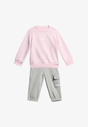 Svetloružová mikina s rebrovanými manžetami a golierom, s bielym logom "adidas". Sivé tepláky s elastickými manžetami, vreckom na cargo a logom.