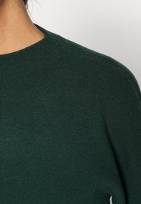 Tummanvihreä villapaita pyöreällä kaula-aukkolla, resorakenteella ja minimalistisella designilla, joka esittelee pehmeää neulottua kangasta.