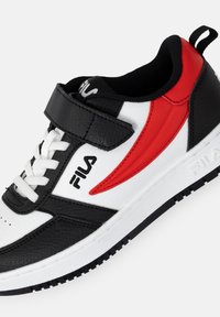 Valkoiset ja mustat synteettiset lenkkarit punaisella korostuksella, joissa on pyöreä kärki, nauhakiinnitys ja tarrakiinnitys, teksturoitu pinta ja brändilogo.