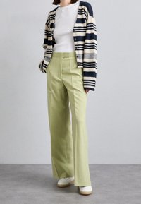 Green wide-leg trousers with front pleats, paired with a white shirt and navy striped cardigan. Smooth fabric and casual style.