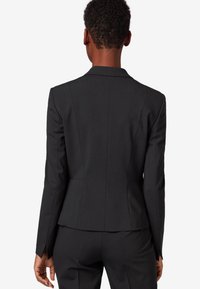 Black tailored blazer with a fitted design. Features a notched collar, structured seams, and smooth fabric. No visible hardware or accents.