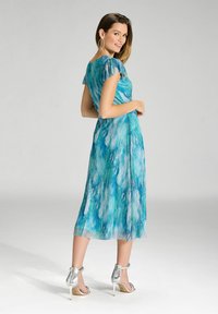 Niebieska i zielona sukienka z falującymi rękawami i swobodnym krojem. Połączona z srebrnymi sandałami na wysokim obcasie.