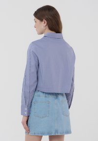 Camicia a righe blu e bianche, tagliata, con colletto e polsini bottonati, abbinata a una gonna di jeans chiaro con tasche posteriori e vita elastica.