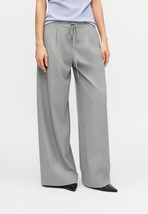 Sivo široke hlače od teksturiranog tkanja, s elastičnim pojasom i glatkim završetkom. Uparene s crnim šiljastim cipelama.